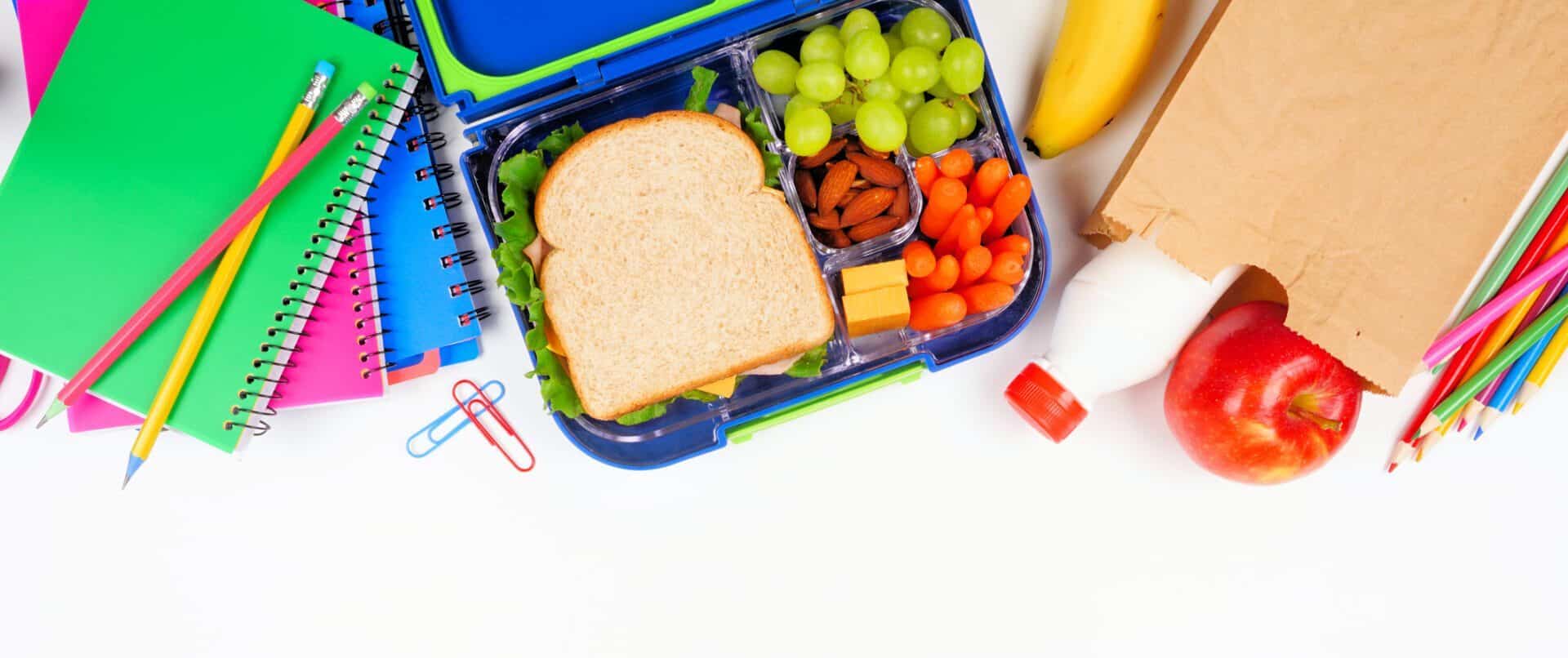 Healthy school lunch with school supplies. Above view top border on a white background.