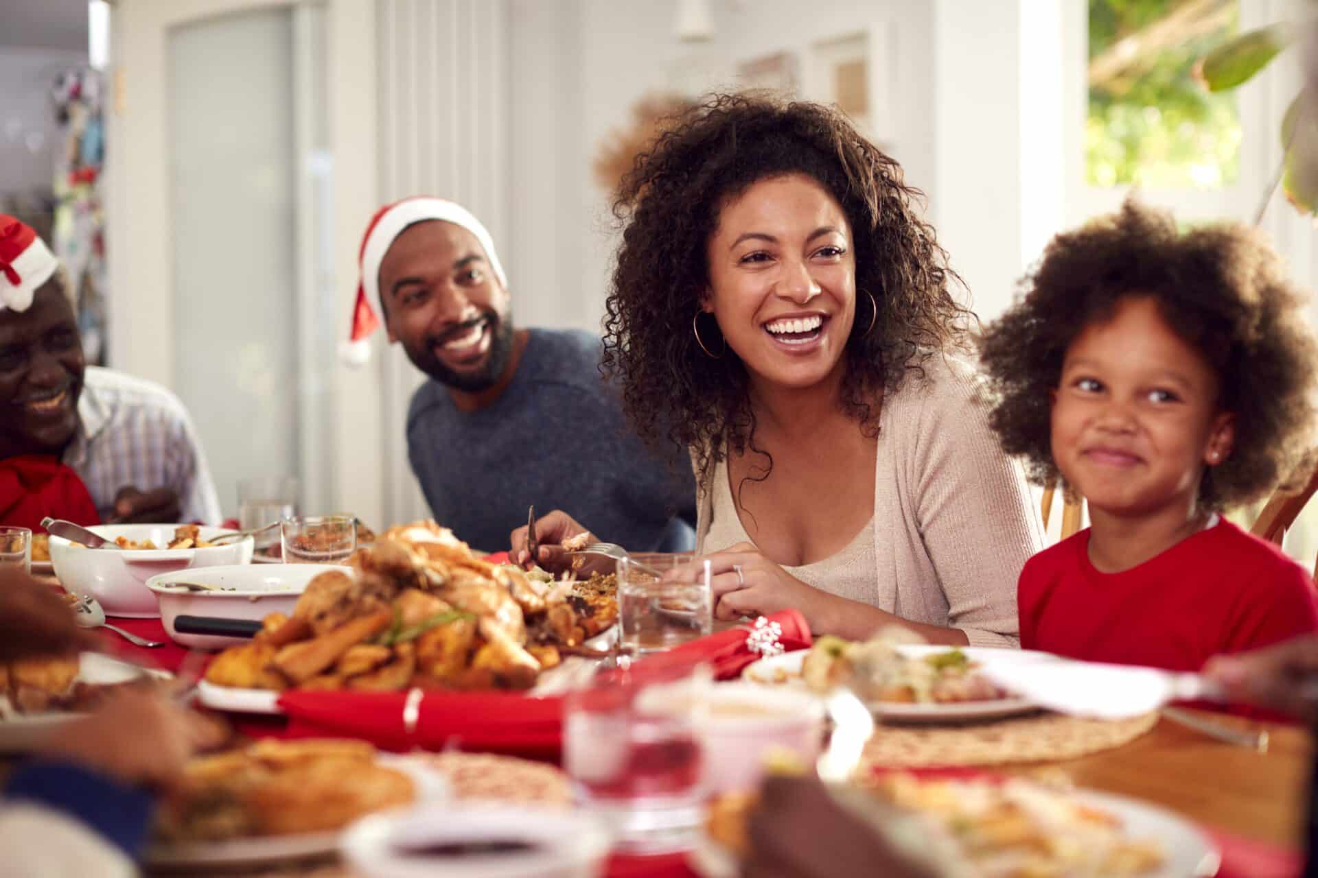 Multi Generation Family In Paper Hats Enjoying Eating Christmas Meal At Home Together