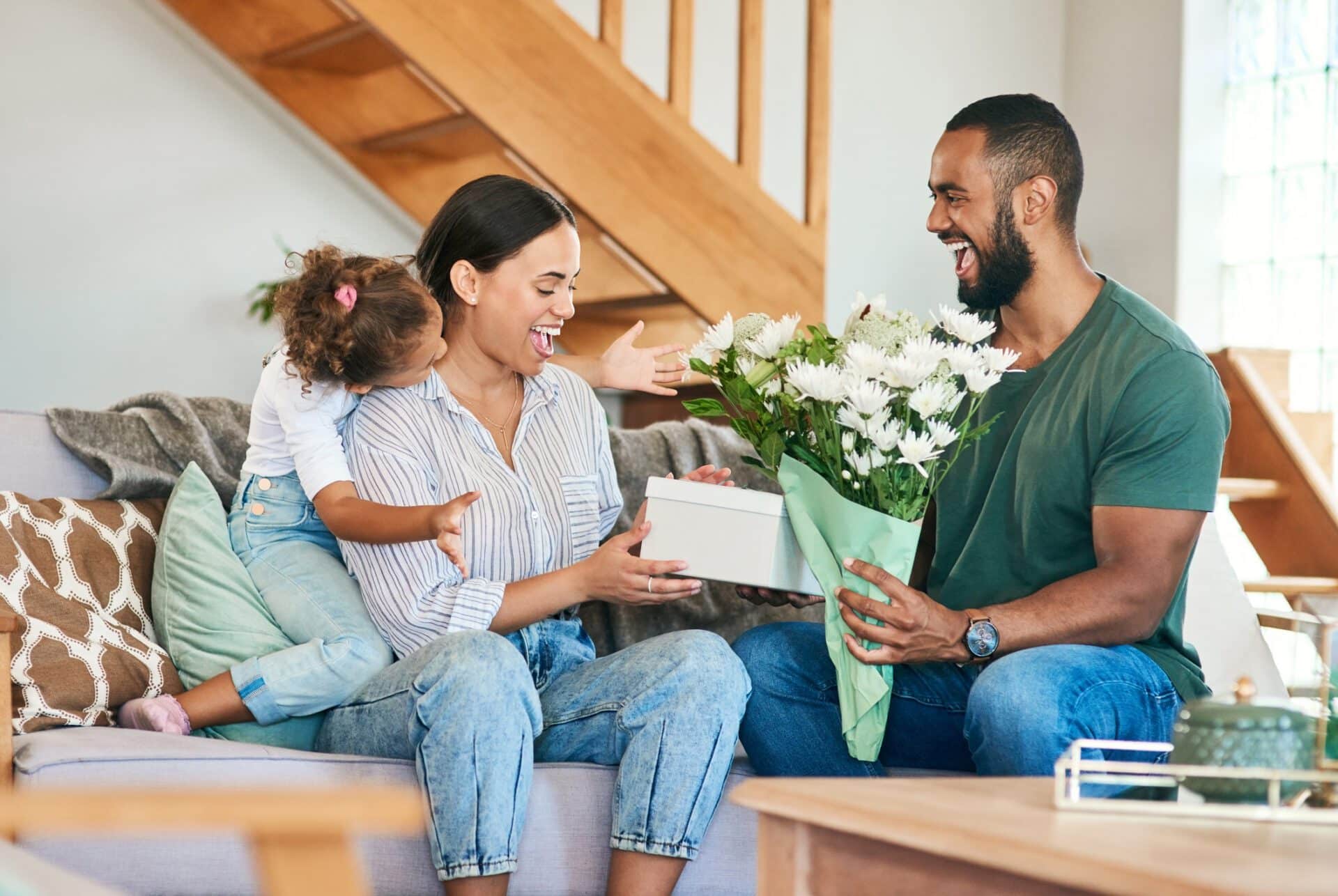 Woman getting a gift and bouquet of flowers from her husband and little daughter at home