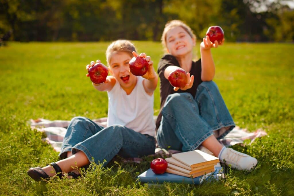 classmates play with red apples on green grass in park