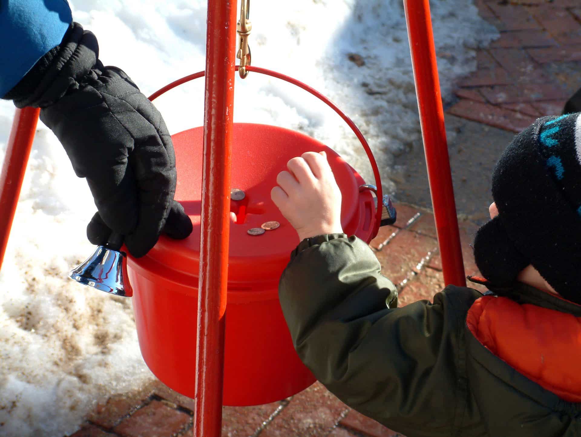 Boy donates coins in a red kettle during holiday season